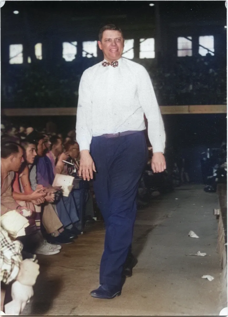 Charley Meyer in a white shirt and bow tie, smiling as he walks past a packed crowd